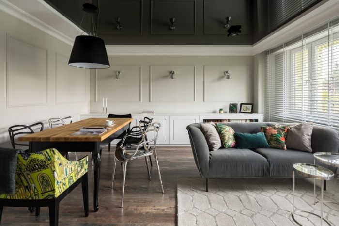 "Image of a living room with a black lacquer ceiling. The glossy surface reflects light, creating a sense of depth in the room. Minimalist furniture and neutral walls enhance the modern aesthetic. Soft lighting fixtures add warmth to the space."