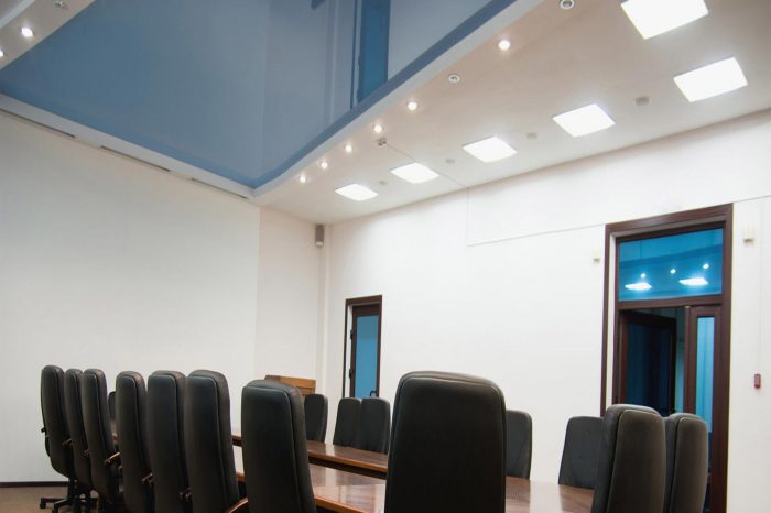 "Conference hall featuring a vibrant blue lacquer stretch ceiling, adding a dynamic touch to the space. The glossy surface interacts with ambient light, illuminating the room with a sense of vibrancy. Professional seating arrangements and modern décor complement the contemporary setting, ideal for meetings and events."