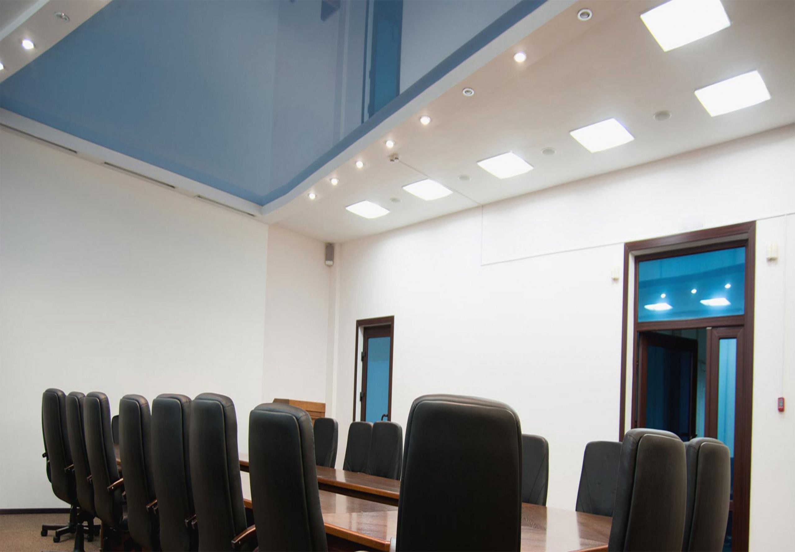 "Conference hall featuring a vibrant blue lacquer stretch ceiling, adding a dynamic touch to the space. The glossy surface interacts with ambient light, illuminating the room with a sense of vibrancy. Professional seating arrangements and modern décor complement the contemporary setting, ideal for meetings and events."